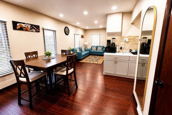 Open-plan living space with dining table, blue sofa, kitchen with white cabinetry, and hardwood floors throughout.